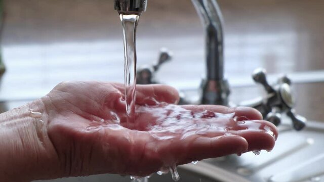 Drinking water from the tap flows into the woman's hand