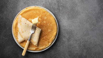stack of pancakes on a plate with butter on a dark gray background, top view,maslenitsa