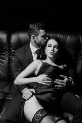 Monochrome shot of man in suit touching sensual woman in dress on couch isolated on black