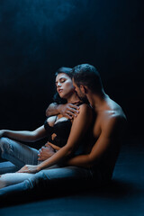Shirtless man kissing brunette girlfriend on black background with smoke