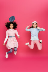 excited interracial girls in stylish spring outfit levitating on pink