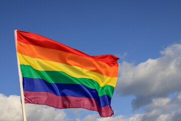 Waving gay pride rainbow flag in blue summer sky, copy space. Realistic flag of LGBT organization include lesbians, gays, bisexuals and transgender.