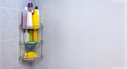 A metal bathroom grate shelf filled with body and hair care products weighs on a blue tile in the corner.