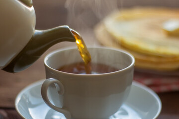 Tea is poured into a breakfast cup with pancakes.