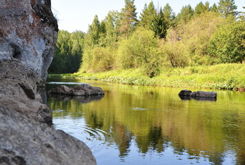 Fototapeta na wymiar Two banks of the river, one with forest and green grass, the other with rocks and rocks.