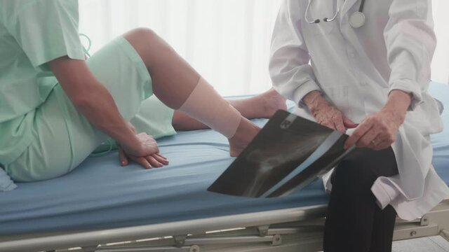 Doctor is specialist diagnosis about disease of bone leg with injured of patient while worried with x-ray film on bed, woman with expertise examining illness, medical and health care concept.