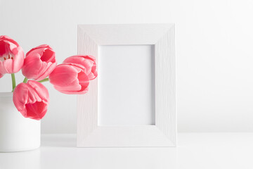White frame mockup with tulips, pink spring flowers in vase on white table. Front view. Place for text, copy space, mockup