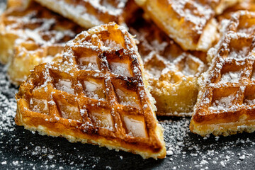 Fresh homemade sweet waffles in the shape of a heart, with powdered sugar. Close up on black surface.