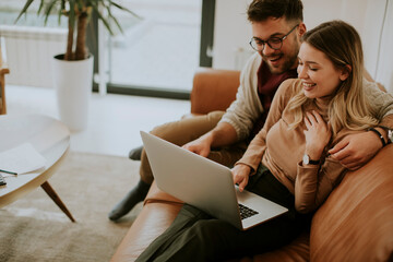 Young couple using laptop together while sitting on sofa at home