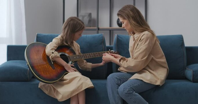 first lesson of guitar playing of little girl, woman teacher is teaching child, demonstrating fingers position on strings