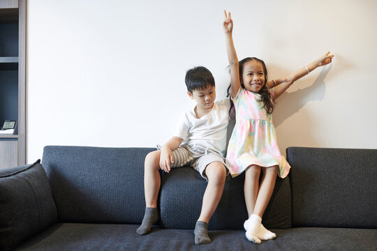 Happy preteen Asian brother and sister playing on sofa at home