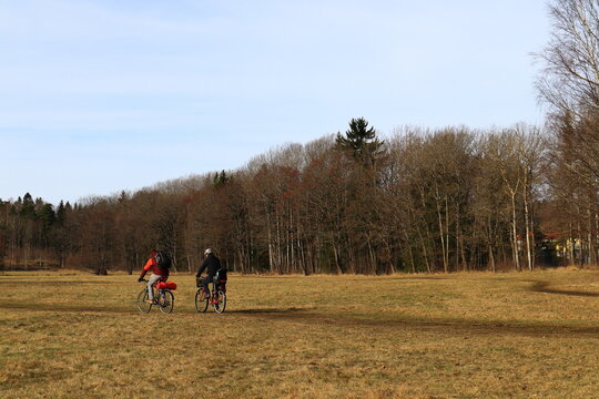 Two Swedish men riding bikes at a large meadow during the spring. Nice landscape photo. A forest in the background. Stockholm, Sweden, Europe.