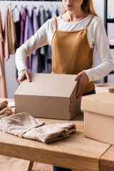 partial view of seller packing carton boxes in clothes showroom, blurred foreground