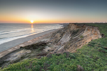 Coastal cliffs with a low sun at sunset showing sea, low tide sand bars,  erosion and  near Barton-on-Sea 