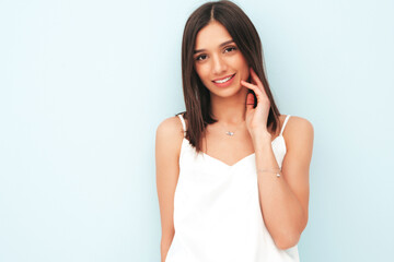 Fototapeta premium Portrait of beautiful smiling woman dressed in white pajamas. Sexy carefree cheerful model enjoying her morning. Adorable and positive female posing near light blue wall in studio. Tanned and skinny
