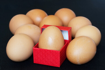 A red gift box with a chicken egg lies on a dark background next to other eggs. A selection of the best foods for Easter. An unusual gift and surprise