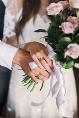 hands of the bride and groom with rings hold the bride's bouquet
