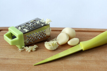 Fresh garlic cloves, knife and grater on an old wooden cutting board.
