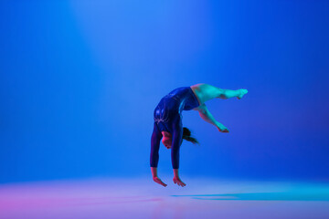 Energy. Young flexible girl isolated on blue studio background in neon light. Young female model...