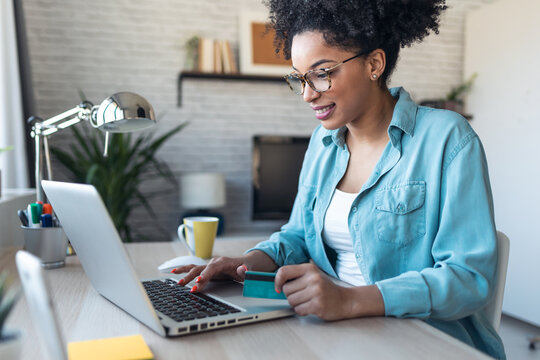 Pretty young afro woman shopping online with credit card with laptop while working on office at home.