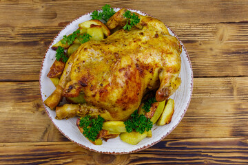 Baked whole chicken with potato on a wooden table. Top view