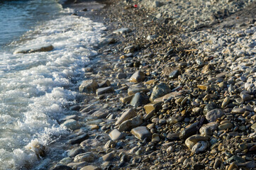 pebble stones on the sea beach, the rolling waves of the sea with foam