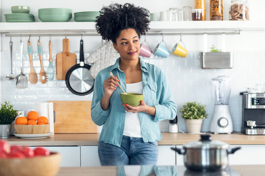 Beautiful Afro Woman Eating Noodles With Chopsticks While Standing In The Kitchen At Home.