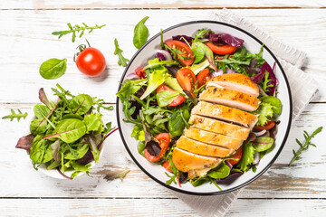 Green salad with baked chicken breast at white kitchen table. Healthy food, clean eating concept. Top view image.