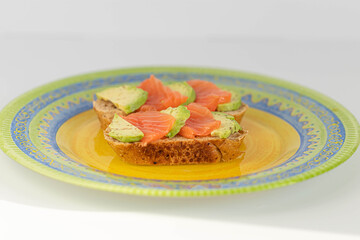 Homemade toast sandwich with salmon and avocado on a slice of cereal bread. The toast lies on a bright yellow plate. healthy food