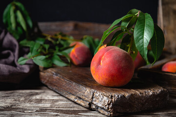 Juicy ripe peach on dark wooden rustic cutting board. Delicious farm peaches with leaves. Still life peach with copy space in dark key. Wooden table with ripe peach fruit.