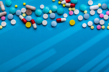 A lot of multi-colored pills on blue background with free space for text, as a concept of medical treatment with a prescription. Painkillers and antibiotics variation, allergy on medicine.
