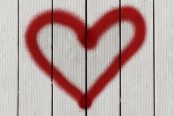 The universally known symbol of love, a heart shape, drawn like a graffiti, in red spray paint, over a set of aged pale wood planks.
