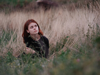 red-haired woman in a black dress lies in a field on dry grass in nature