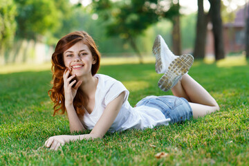 cute red-haired woman lies on the lawn outdoors in the park