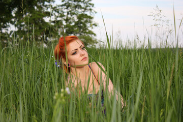 Beautiful young girl with red hair on a green lawn enjoying nature. Harmony concept.