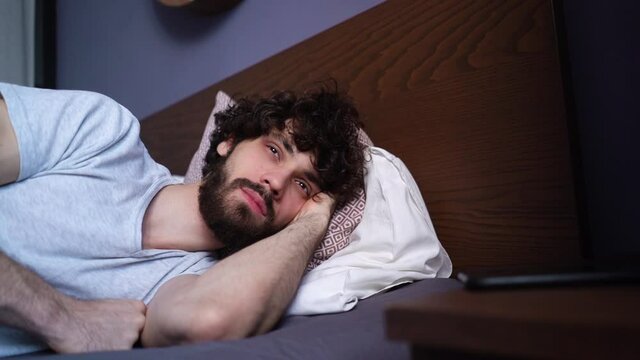 Close-up face of sleeping young man opening eyes, waking up and happy looking away. Handsome bearded male in casual clothes wakes up after an afternoon nap. Handsome bearded male has pleasant dream.