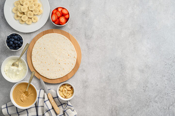 Tortilla cooking process with different fillings of peanut butter, banana, strawberry, blueberry, almond. Food trend. Sweet sandwich for breakfast. Trendy way of wrapping. Top view, copy space