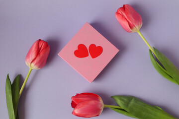 Pink gift box with two red hearts, scarlet poppies around, pastel background, top view