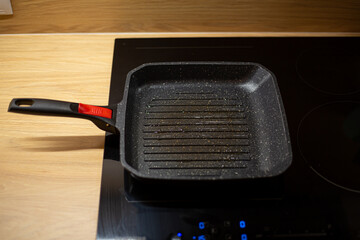 Black oily grill pan is heating on electrical ceramic hob for burger cooking at home