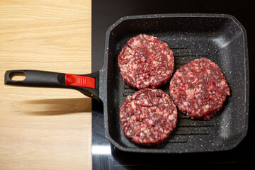 Burger raw minced beef meat cutlet on a grill pan. Process of cooking self made burgers at home