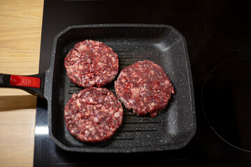 Burger raw minced beef meat cutlet on a grill pan. Process of cooking self made burgers at home