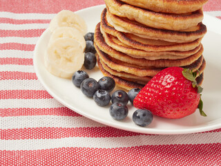 Close-up of delicious pancakes, with fresh blueberries, strawberries and maple syrup on a light background. With space to copy. Sweet maple syrup flows from a stack of pancakes