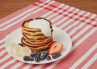 Close-up of delicious pancakes, with fresh blueberries, strawberries and maple syrup on a light background. With space to copy. Sweet maple syrup flows from a stack of pancakes
