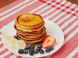 Close-up of delicious pancakes, with fresh blueberries, strawberries and maple syrup on a light background. With space to copy. Sweet maple syrup flows from a stack of pancakes