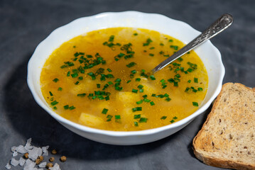 Chicken or beef broth with potatoes and green onions in a white bowl with a spoon, slices of bread and spices. Close-up. Place for your text.