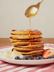 Close-up of delicious pancakes, with fresh blueberries, strawberries and maple syrup on a light background. With space to copy. Sweet maple syrup flows from a stack of pancakes
