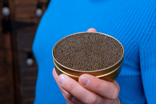 beluga or sturgeon black caviar in hand, a blurry man holding a black caviar jar in the background, photo with a small depth of field