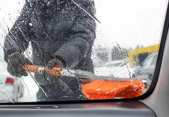 A man brushes a car glass from water and snow. View from inside the car. Blurred image. Selective focus.