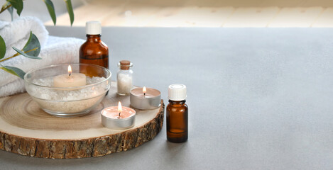 Aromatherapy concept with essential oil bottle, cotton flowers, burning candles on grey background. Spa or herbal medicine still life composition. Resort concept. Copyspace.