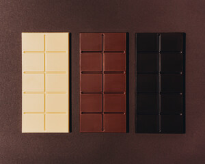 Variety of chocolate bars on brown background. Dark chocolate, milk chocolate, white chocolate